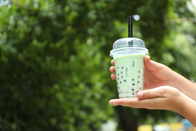 Photo of Woman with tasty milk bubble tea in plastic cup outdoors, closeup. Space for text