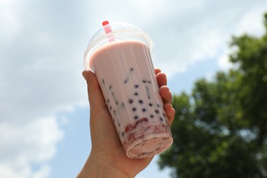 Photo of Woman with tasty milk bubble tea in plastic cup outdoors, closeup