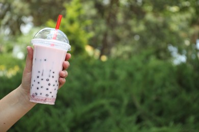 Photo of Woman with tasty milk bubble tea in plastic cup outdoors, closeup. Space for text