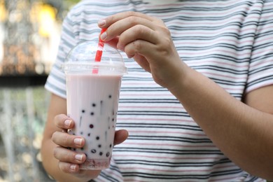 Photo of Woman with tasty milk bubble tea in plastic cup outdoors, closeup