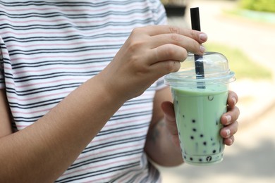 Photo of Woman with tasty milk bubble tea in plastic cup outdoors, closeup