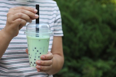 Photo of Woman with tasty milk bubble tea in plastic cup outdoors, closeup. Space for text