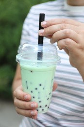 Photo of Woman with tasty milk bubble tea in plastic cup outdoors, closeup