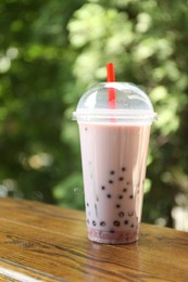 Photo of Tasty milk bubble tea in plastic cup on wooden table