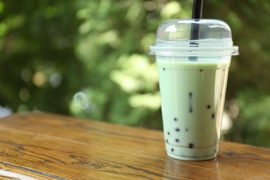 Photo of Tasty milk bubble tea in plastic cup on wooden table. Space for text