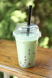 Photo of Tasty milk bubble tea in plastic cup on wooden table