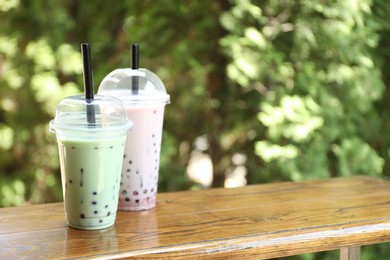 Photo of Tasty milk bubble tea in plastic cups on wooden table. Space for text