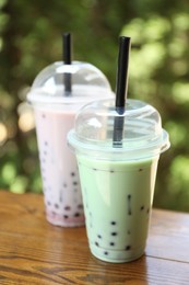 Photo of Tasty milk bubble tea in plastic cups on wooden table, closeup