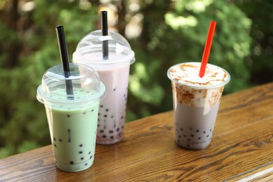 Photo of Tasty milk bubble tea in plastic cups on wooden table