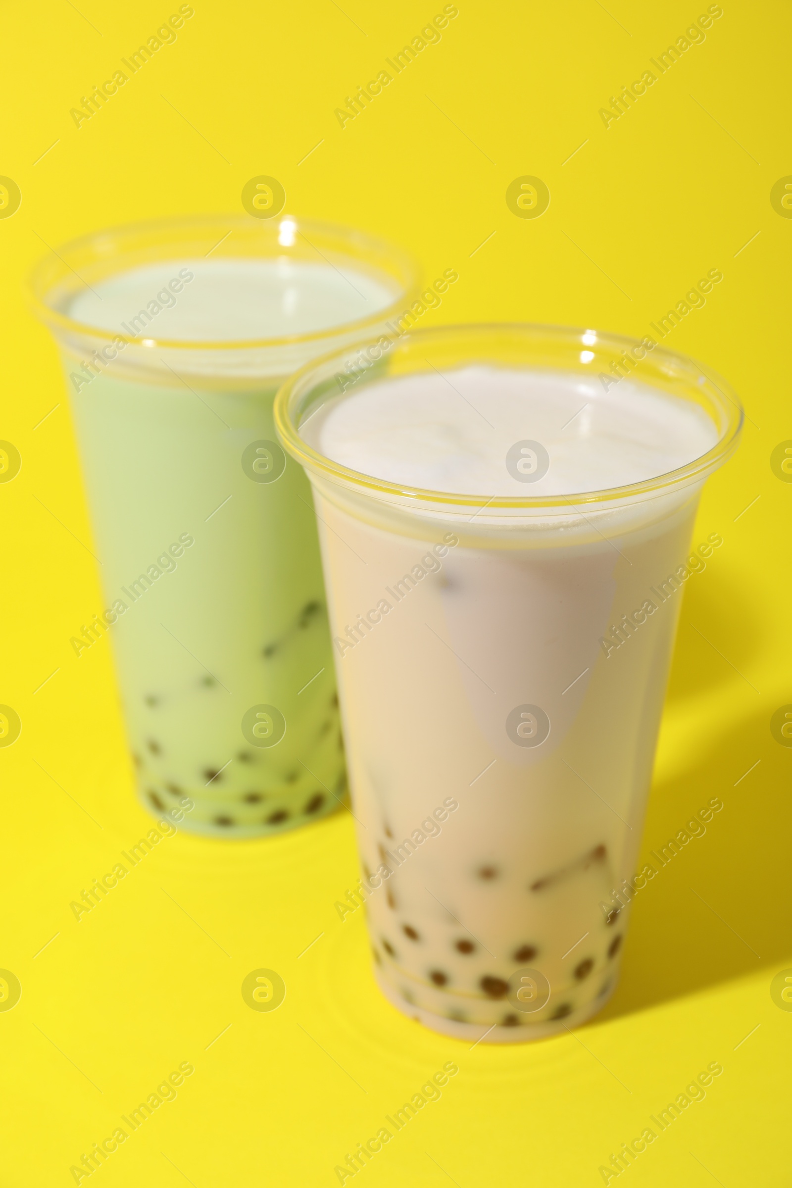 Tasty milk bubble tea in plastic cups on yellow background Photo of Tasty milk bubble tea in plastic cups on yellow background