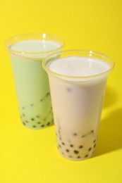 Photo of Tasty milk bubble tea in plastic cups on yellow background