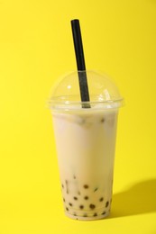 Photo of Tasty milk bubble tea in plastic cup on yellow background