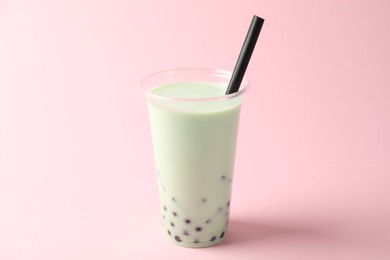 Photo of Tasty milk bubble tea in plastic cup on pink background