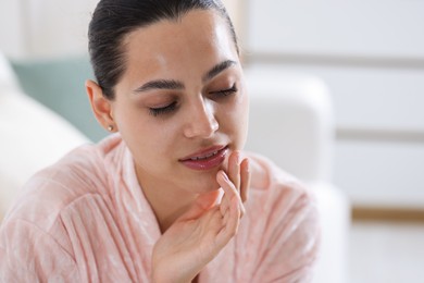 Photo of Young woman with lip balm at home