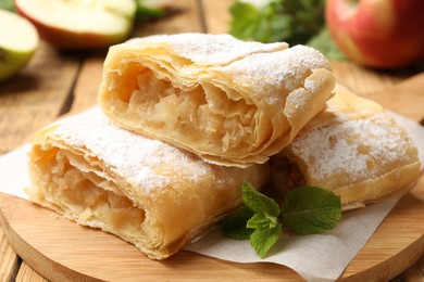 Photo of Pieces of tasty apple strudel with powdered sugar and mint on wooden table, closeup