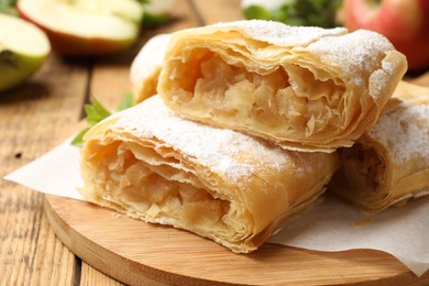Photo of Pieces of tasty apple strudel with powdered sugar on wooden table, closeup