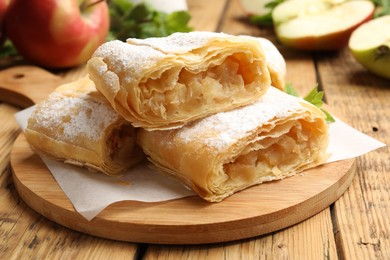 Photo of Pieces of tasty apple strudel with powdered sugar on wooden table, closeup