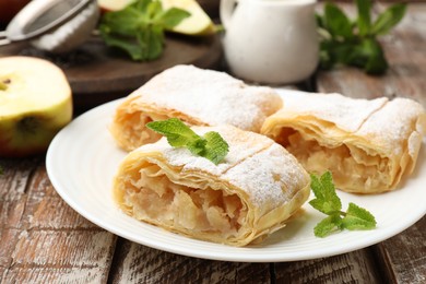 Photo of Pieces of tasty apple strudel with powdered sugar and mint on wooden table, closeup