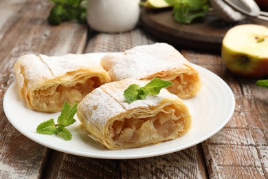 Photo of Pieces of tasty apple strudel with powdered sugar and mint on wooden table, closeup