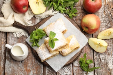Photo of Pieces of tasty apple strudel with powdered sugar, mint and fruits on wooden table, flat lay