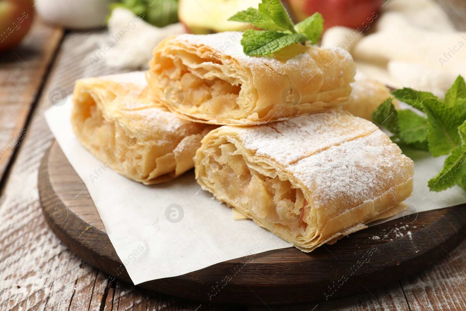 Pieces of tasty apple strudel with powdered sugar, mint and fruits on wooden table, closeup Photo of Pieces of tasty apple strudel with powdered sugar, mint and fruits on wooden table, closeup