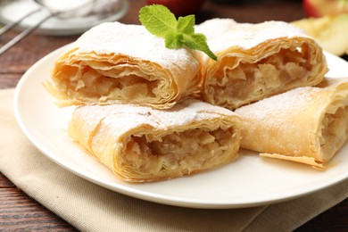 Photo of Pieces of tasty apple strudel with powdered sugar and mint on wooden table, closeup