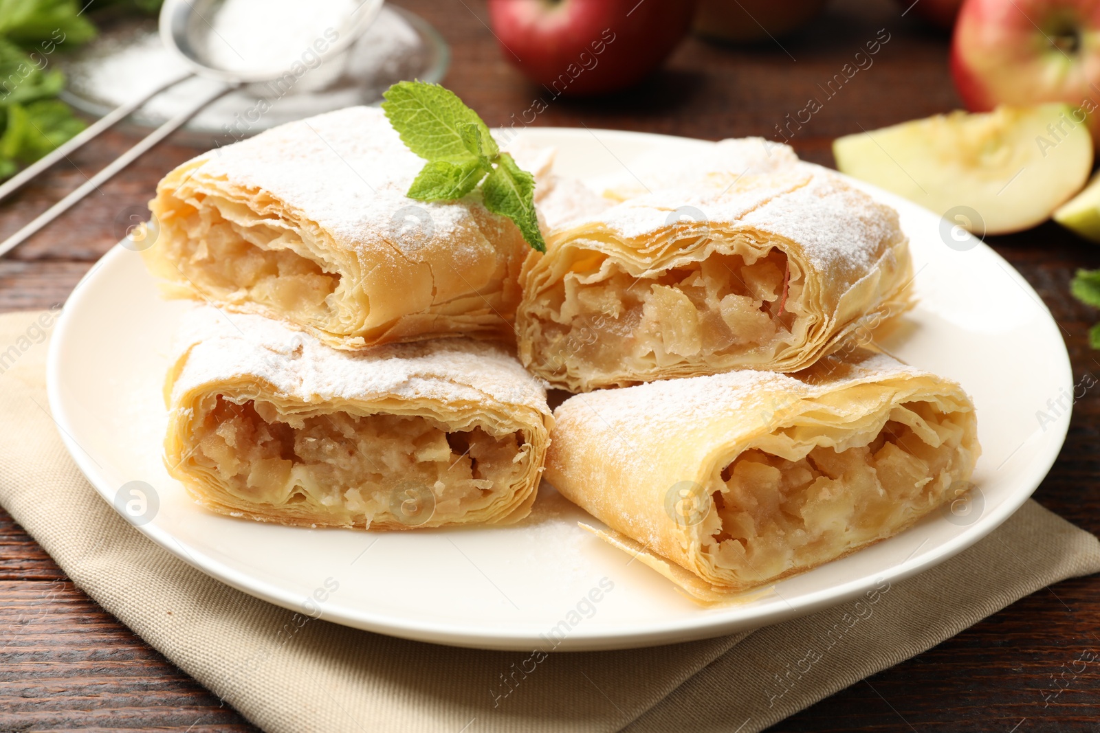Pieces of tasty apple strudel with powdered sugar and mint on wooden table, closeup Photo of Pieces of tasty apple strudel with powdered sugar and mint on wooden table, closeup