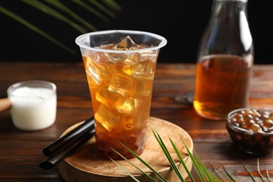 Photo of Tasty iced bubble tea and ingredients on wooden table