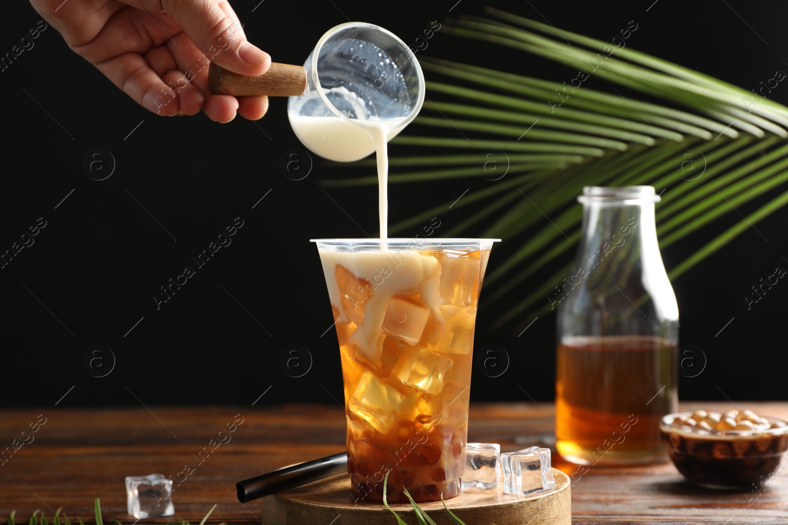 Woman pouring milk into bubble tea at wooden table, closeup Photo of Woman pouring milk into bubble tea at wooden table, closeup
