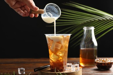 Photo of Woman pouring milk into bubble tea at wooden table, closeup
