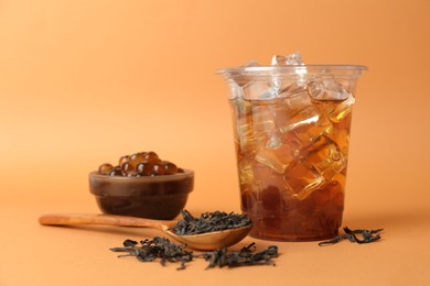 Photo of Tasty iced bubble tea and ingredients on orange background