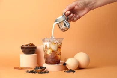 Photo of Woman pouring milk into bubble tea on orange background, closeup