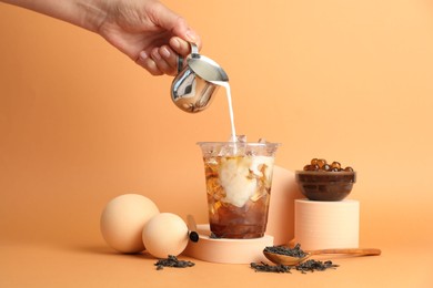 Photo of Woman pouring milk into bubble tea on orange background, closeup