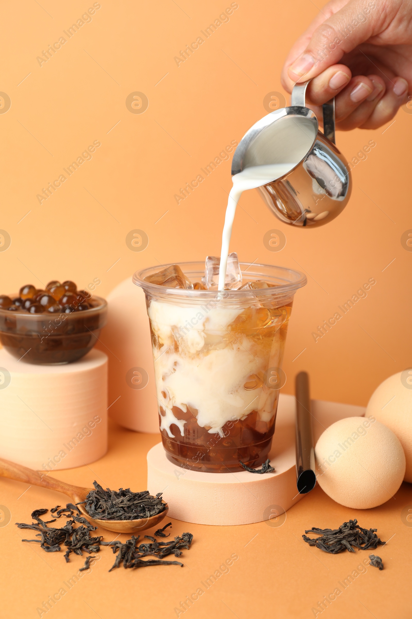 Woman pouring milk into bubble tea on orange background, closeup Photo of Woman pouring milk into bubble tea on orange background, closeup
