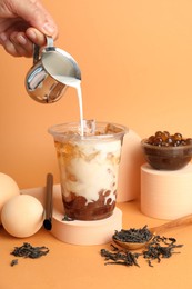 Photo of Woman pouring milk into bubble tea on orange background, closeup