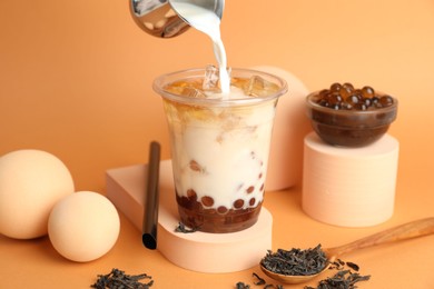 Photo of Pouring milk into bubble tea on orange background, closeup