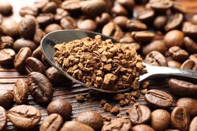 Photo of Spoon with instant coffee and beans on wooden table, closeup