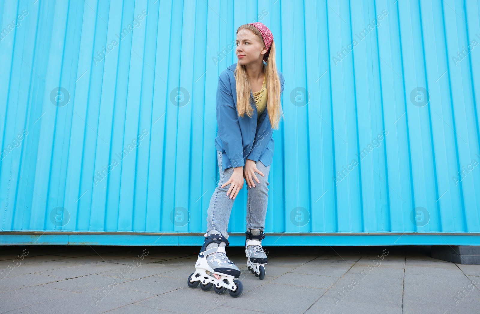 Beautiful young woman with roller skates near light blue wall outdoors, low angle view Photo of Beautiful young woman with roller skates near light blue wall outdoors, low angle view