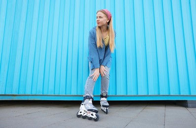 Photo of Beautiful young woman with roller skates near light blue wall outdoors, low angle view