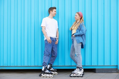 Photo of Happy couple with roller skates near light blue wall outdoors