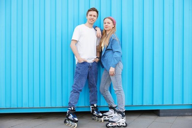 Photo of Happy couple with roller skates near light blue wall outdoors