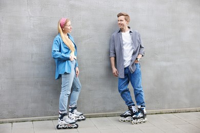 Photo of Happy couple with roller skates near gray wall outdoors