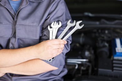 Photo of Auto parts. Professional mechanic with different wrenches near open hood of car indoors, closeup. Space for text