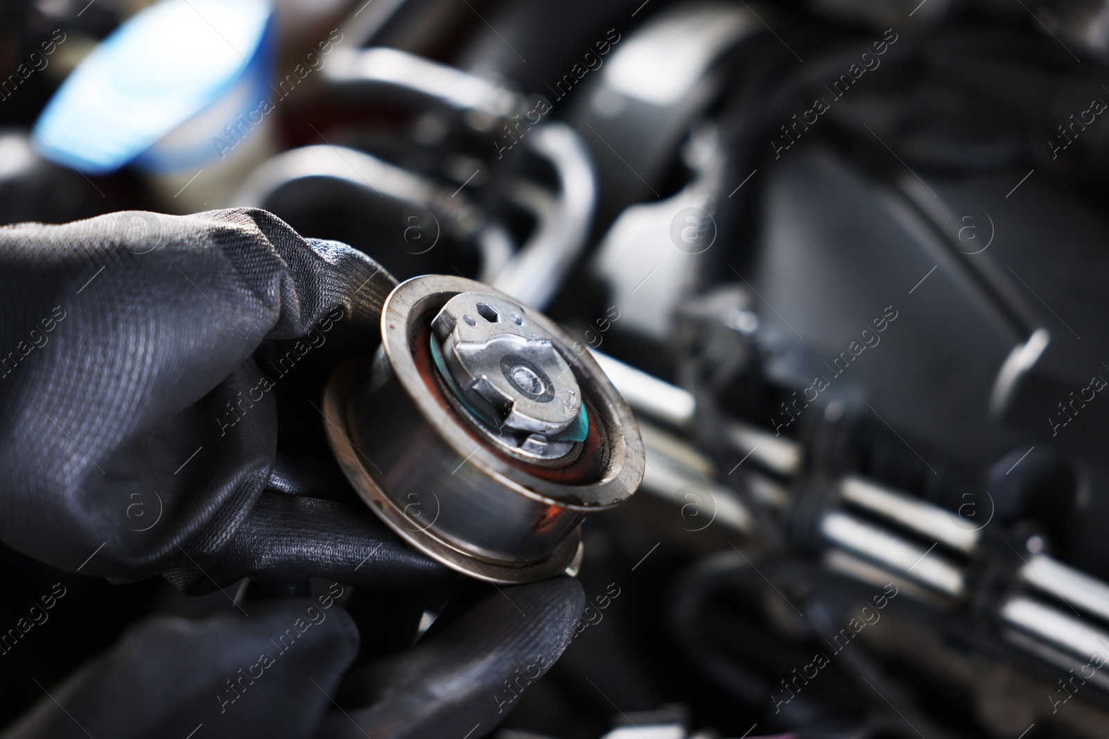 Auto part. Professional mechanic with idler-wheel near open hood of car indoors, closeup. Space for text Photo of Auto part. Professional mechanic with idler-wheel near open hood of car indoors, closeup. Space for text