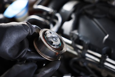 Photo of Auto part. Professional mechanic with idler-wheel near open hood of car indoors, closeup. Space for text