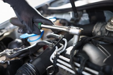 Photo of Auto parts. Professional mechanic with torque wrench fixing car indoors, closeup