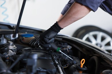 Photo of Auto parts. Professional mechanic with screwdriver fixing car indoors, closeup