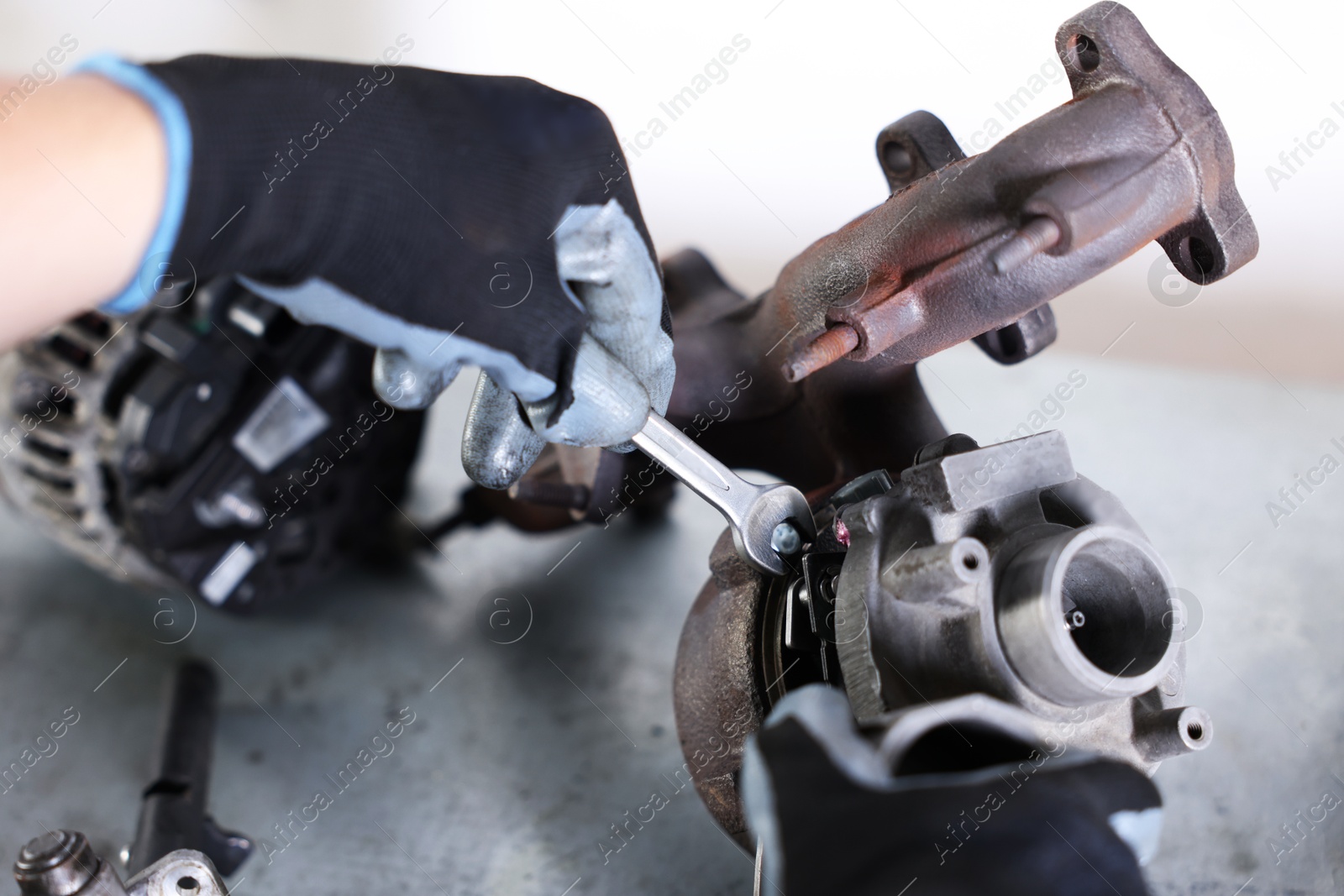 Auto parts. Professional mechanic with wrench fixing turbocharger at grey table indoors, closeup Photo of Auto parts. Professional mechanic with wrench fixing turbocharger at grey table indoors, closeup