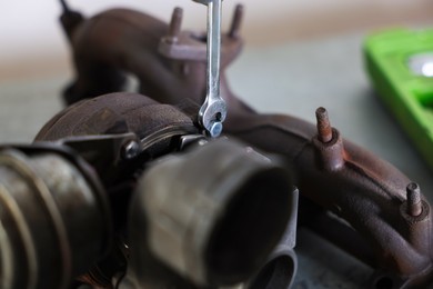 Photo of Auto parts. Fixing turbocharger with wrench at table indoors, closeup