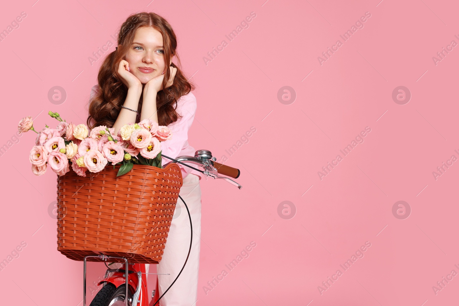 Beautiful teenage girl posing on bicycle with basket of flowers against pink background. Space for text Photo of Beautiful teenage girl posing on bicycle with basket of flowers against pink background. Space for text